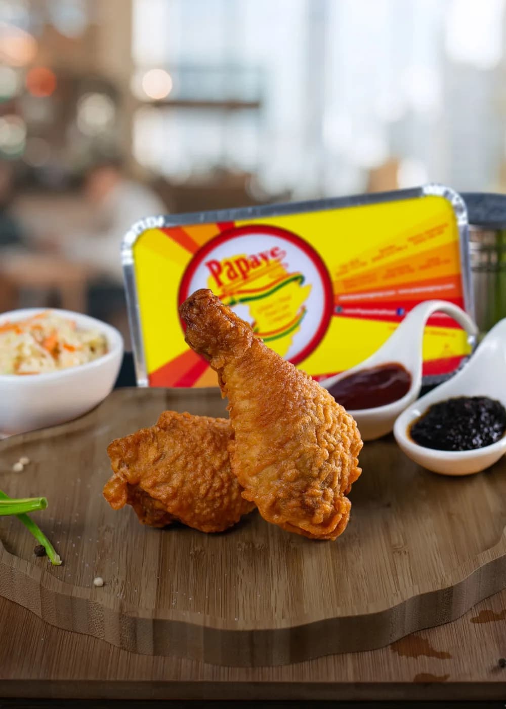 Two pieces of Papaye broasted chicken with coleslaw and sauces, beside a Papaye box